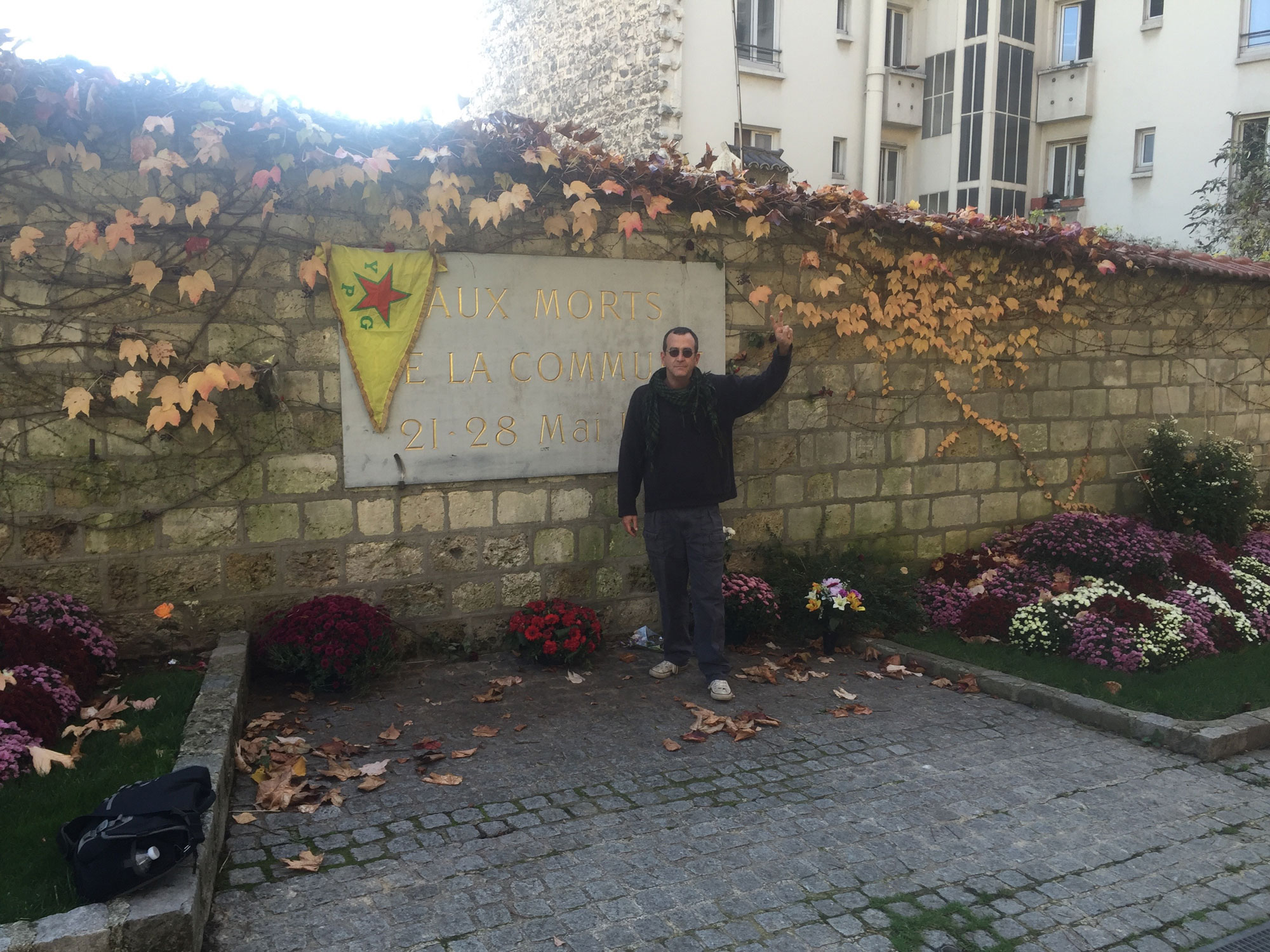 Paul Z. Simons at the Cimetière du Père Lachaise in Paris where the last participants in the Paris Commune were executed, displaying a YPG flag.